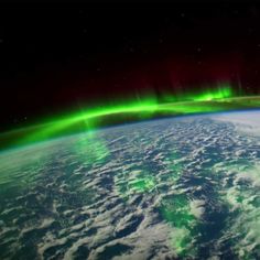 an image of the earth from space with bright green and red lights above it in the distance