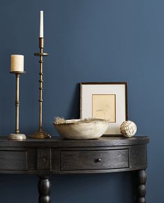 a wooden table topped with a bowl next to a candle and framed pictures on the wall