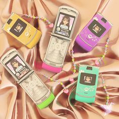 four cell phones are laying on a pink satin surface with beaded necklaces around them