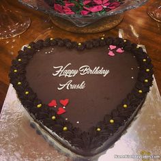 a heart shaped chocolate cake on a table with pink flowers in the center and happy birthday any name here