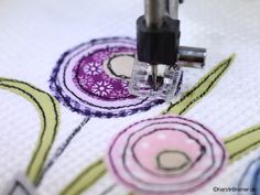 the sewing machine is working on an embroidered fabric with flower designs in purple and green