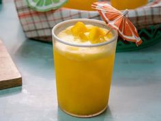 a glass filled with orange juice sitting on top of a table next to an umbrella