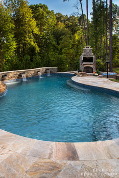 an outdoor swimming pool surrounded by stone steps and patio furniture, with a fireplace in the background