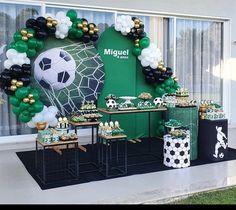 a table topped with lots of green and white balloons next to a wall covered in soccer decorations