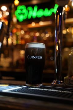 a pint of guinness sitting on top of a table in front of a neon sign