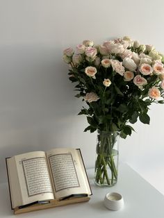 a vase filled with flowers next to an open book on top of a white table