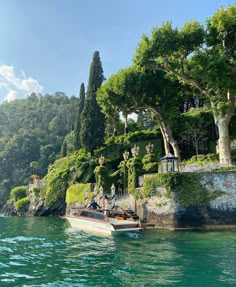 a small boat is on the water near some trees and bushes in front of a cliff