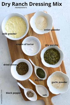 the ingredients for dry ranch dressing in small white bowls on a wooden cutting board with spoons