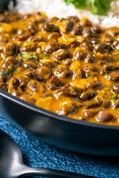 a skillet filled with beans and rice on top of a blue cloth next to a spoon