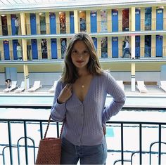 a woman standing in front of a swimming pool holding a purse and posing for the camera