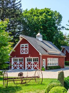 a red barn with two large white doors and an old farm implements in the front yard