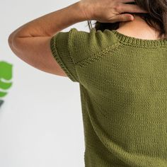 the back of a woman's green sweater with her hands on her head,