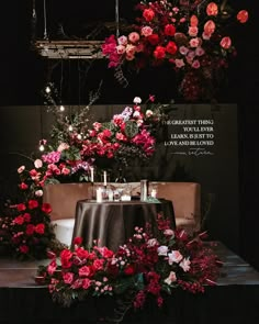 a table topped with flowers and candles under a chandelier filled with pink roses