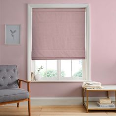 a living room with pink walls and a chair in front of a window that has roman shades on it