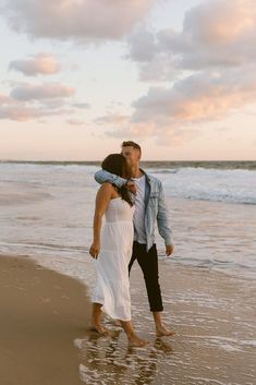 a man and woman are kissing on the beach at sunset with waves coming in behind them