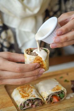 a person is dipping sauce into a burrito with meat and vegetables on it,