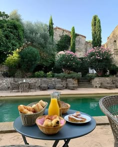 a table that has some food on top of it near a pool with trees and bushes in the background