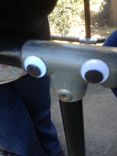 two people standing next to each other near a metal pole with googly eyes on it