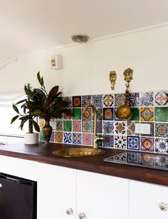 a kitchen with colorful tiles on the backsplash and wooden countertop, along with a potted plant