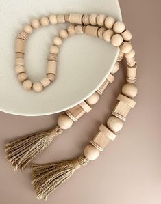 a wooden bead necklace with tassels on a white plate next to it