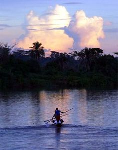 a man riding on the back of a boat across a river under a cloudy sky