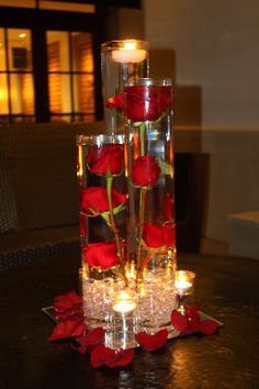 three tall vases with roses and candles on a table