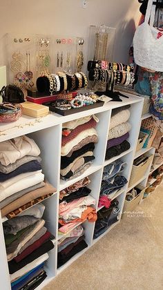 a closet filled with lots of different types of clothes and jewelry on shelves next to a wall