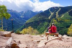 two people sitting on a bench looking at the mountains and valleys in the valley below