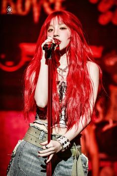 a woman with long red hair and piercings on her head is singing into a microphone