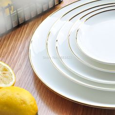 a stack of white plates with gold rims next to a lemon on a wooden table