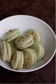 a white bowl filled with green macaroons on top of a table