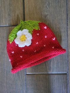 a knitted strawberry hat sitting on top of a wooden floor next to a white flower