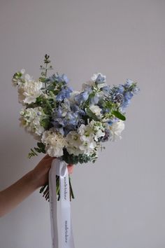 a person holding a bouquet of blue and white flowers with a ribbon tied around it