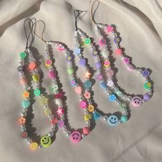 several necklaces with smiley faces and buttons hanging from strings on a white cloth background