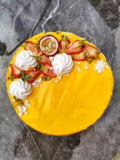 a yellow cake with strawberries and whipped cream on top is sitting on a marble surface