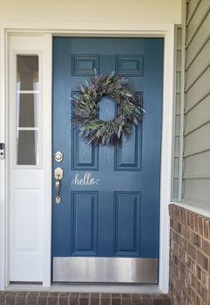 a blue front door with a wreath on it and the word hello written in cursive