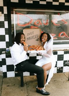 two people sitting on a bench holding up a pizza box with just married written on it