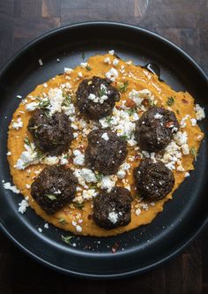 a black plate topped with meatballs covered in cheese