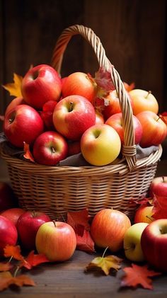 a basket filled with lots of red and yellow apples next to autumn leaves on the ground