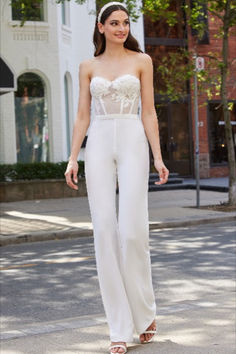 a woman is standing on the street wearing white pants and a strapless bra top