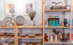 shelves filled with plates and vases on wooden shelves in a room full of pictures