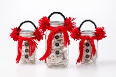 three mason jars filled with buttons and red pom - poms on white background