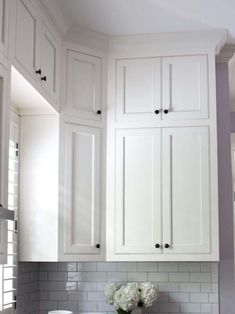 a kitchen with white cabinets and marble counter tops, along with a vase filled with flowers