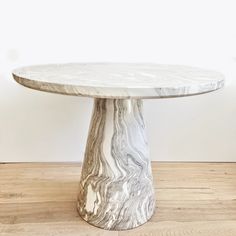 a round marble table on wooden flooring with white wall in the backround