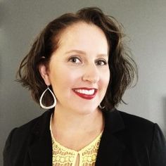 a woman in a black jacket and yellow shirt smiles at the camera with her hand on her hip