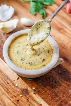 a spoon full of broccoli soup on top of a wooden table next to garlic