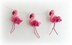 three pink flamingos hanging on a clothes line with pom poms in the shape of balls