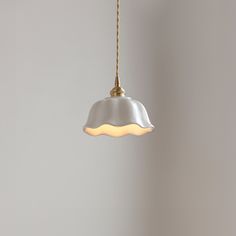 a white light hanging from a gold colored chain on a gray wall in an empty room