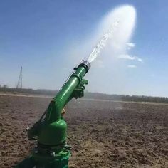 a green fire hydrant spewing water on top of a dirt field in front of a power line