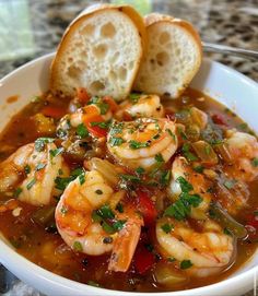 a white bowl filled with shrimp and vegetables next to two pieces of bread on top of a table